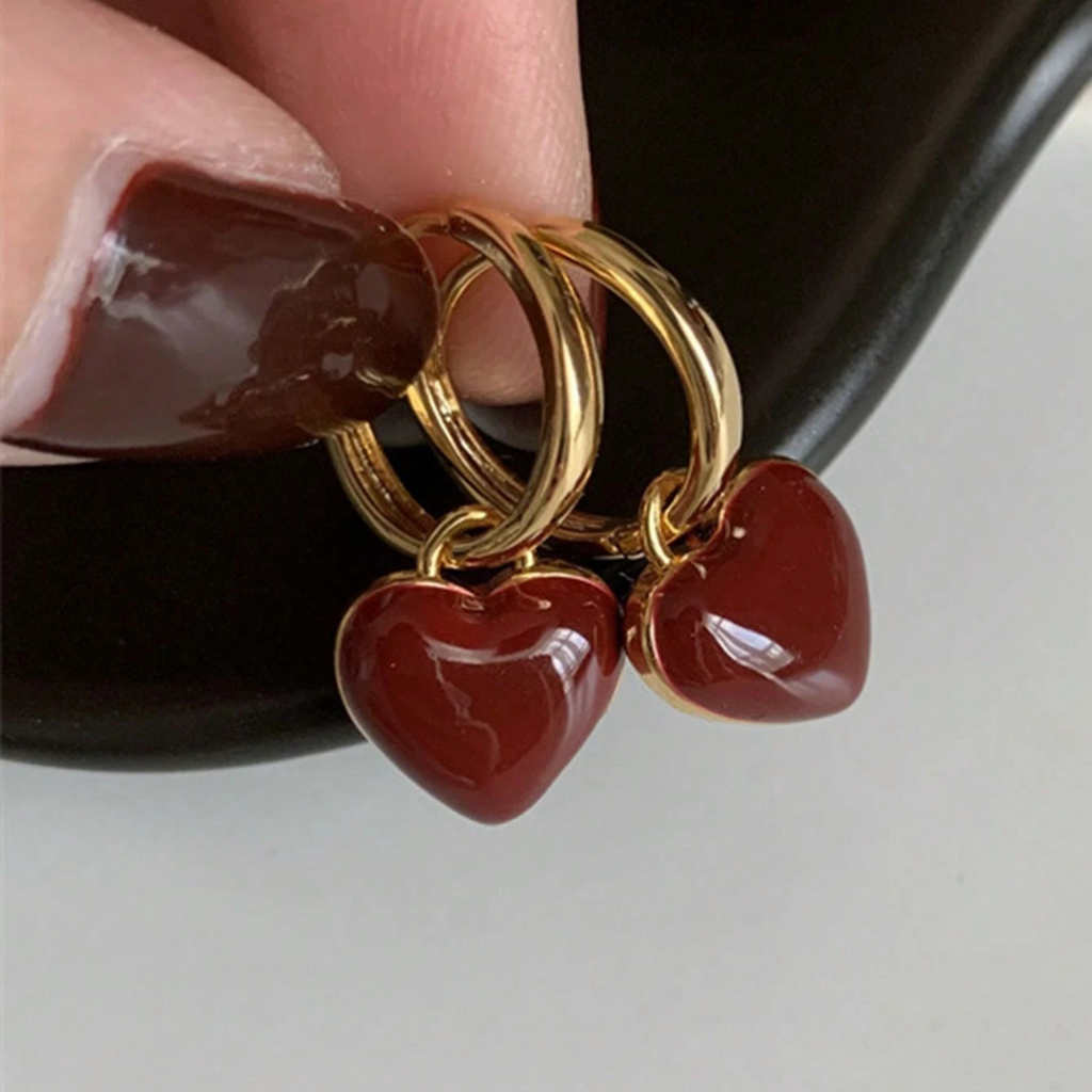 Pendientes de aro dorados con colgante de corazón rojo, de la marca Vega Madrid, mostrando el diseño elegante y brillante.