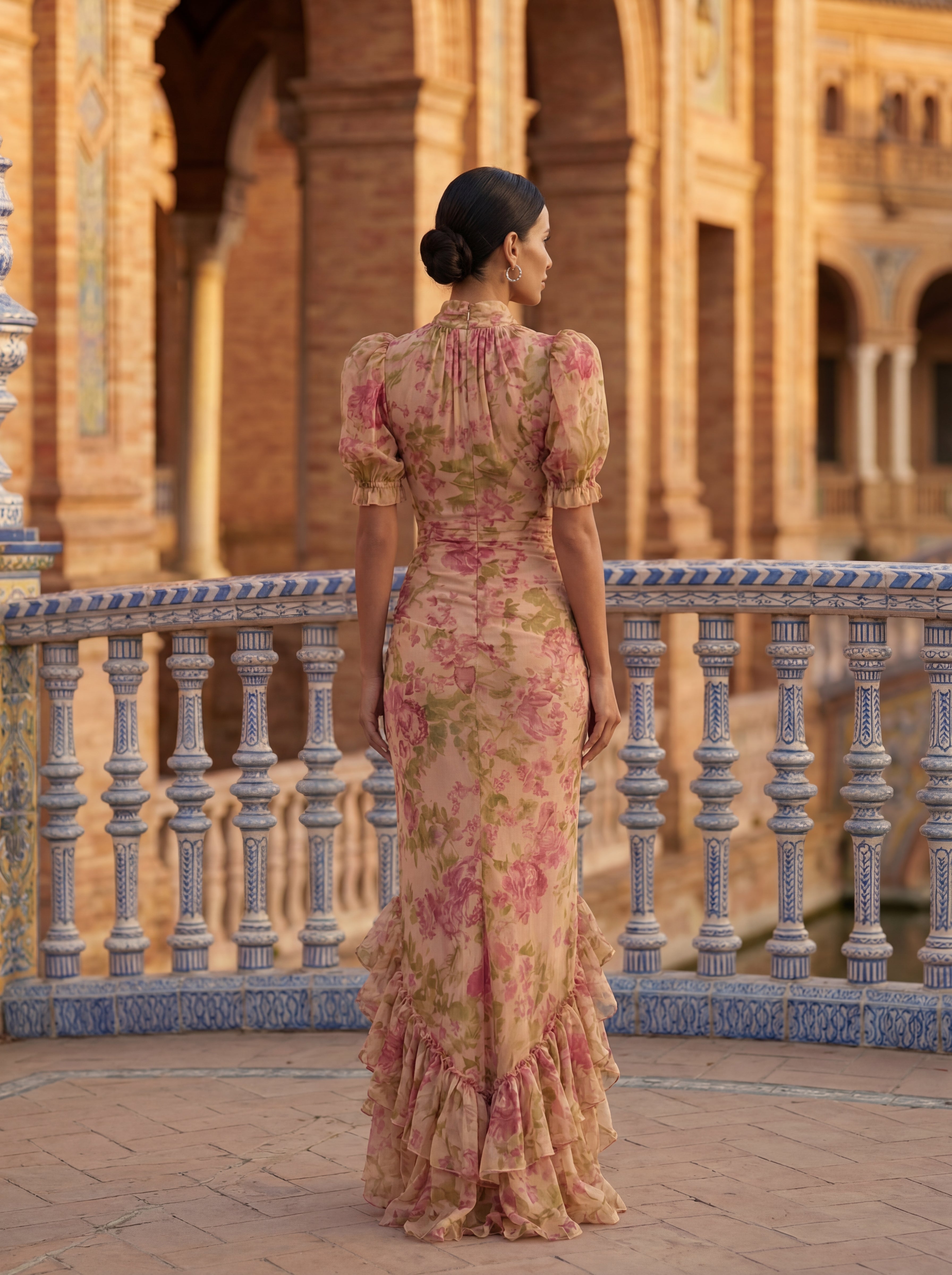 Mujer con vestido largo floral Vega Madrid Noelia, cuello alto y detalles de volantes, en un fondo neutro.